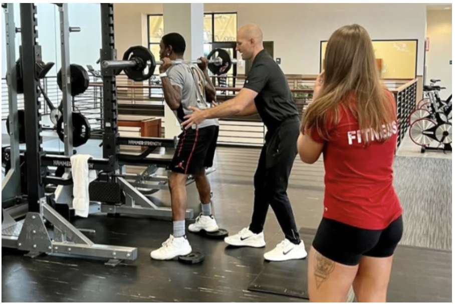 Matthew coaching a barbell squat in a gym