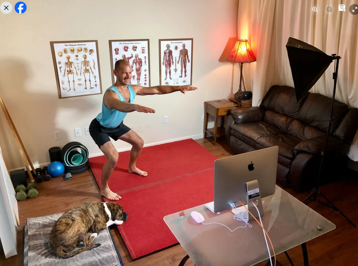 Matthew demonstrating a squat in his home training space, with a computer in front of him